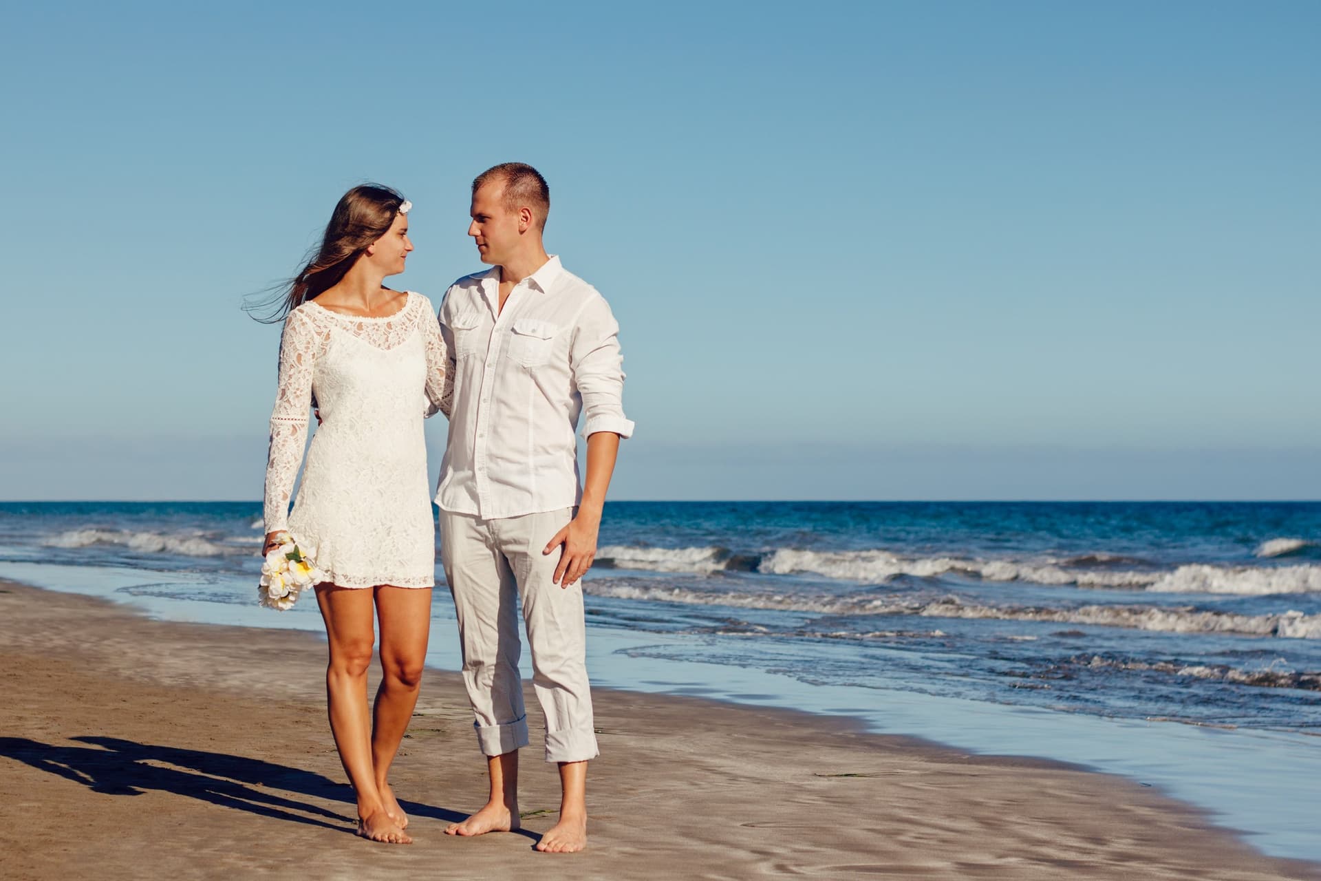 Koppel loopt blootsvoets over het strand in witte kleding